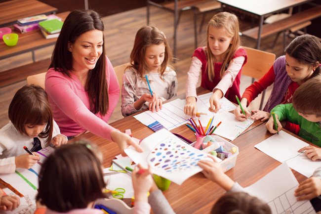 professora sorrindo em uma sala de aula com quatro crianças sorrindo, todas elas concentradas em um livro desenhado que a professora está mostrando. A sala de aula pode ter carteiras, quadro-negro, janelas e decorações temáticas de educação infantil. A professora pode estar apontando para alguma parte do livro enquanto as crianças estão olhando atentamente para as ilustrações. O clima é alegre e descontraído, com uma sensação de aprendizado divertido e envolvente.